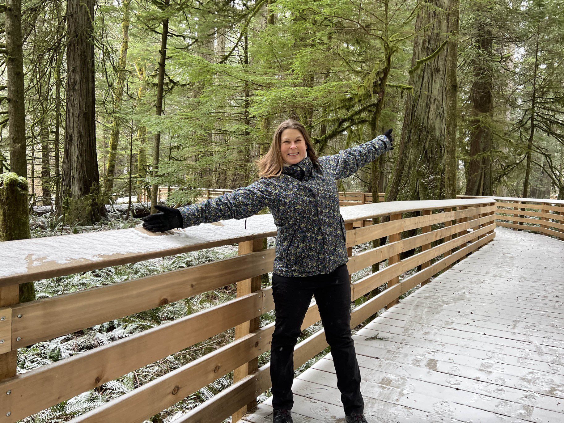 women in blue jacket with arms outstretched in the winter forest